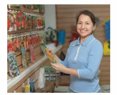 Assia devant les graines de carottes Assia, souriante, tenant un sachet de graines devant un présentoir de graines de légumes — exercice de maths en 2de sur les inéquations